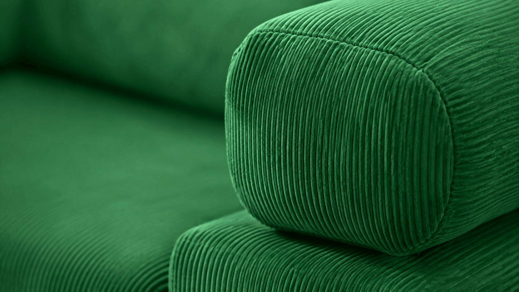 Close-up of a green corduroy sofa cushion showing the ribbed fabric texture and upholstered arm detail.